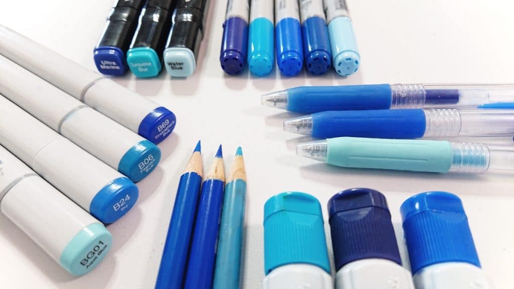 different types of blue coloured pens, pencils, and markers on a white table