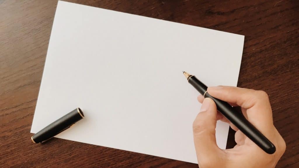 holding ballpoint pen with a blank paper on the table