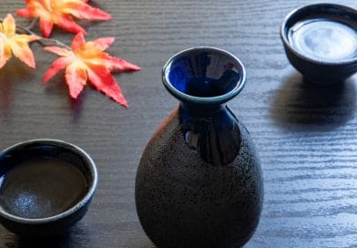 a sake bottle and two glassess on a wooden table with an autumn leaf