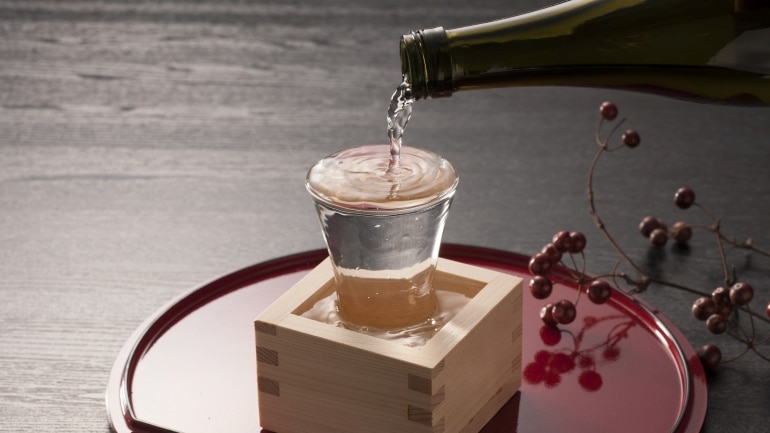 puring sake into a small glass inside a square-shaped wooden cup