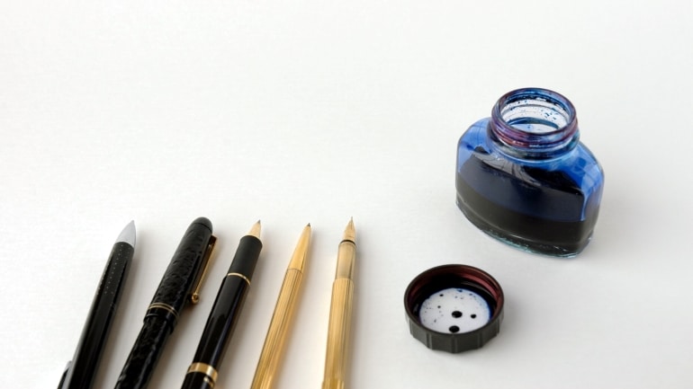 an ink bottle next to different types of pens on a white table